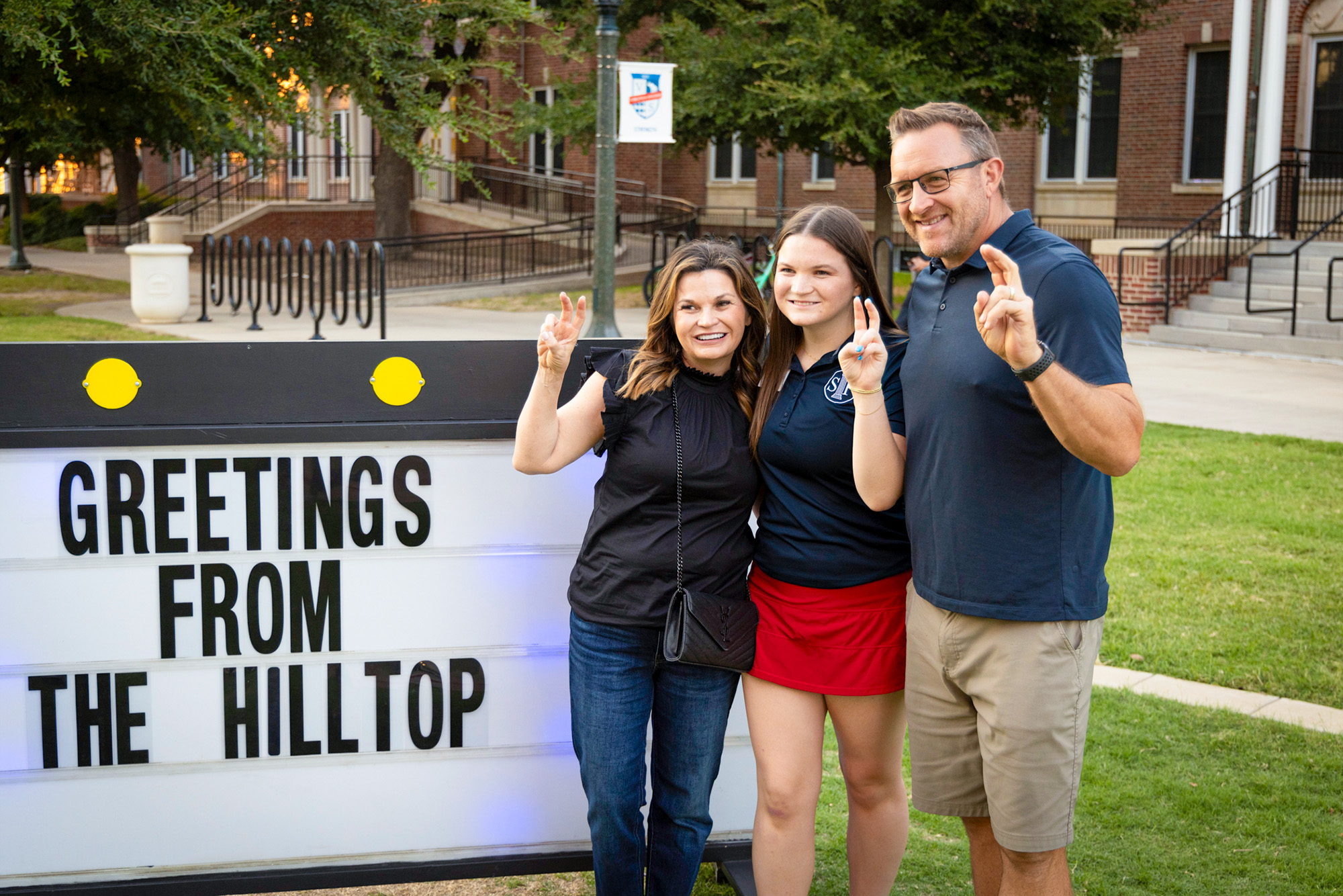 Parents and Students at Family Weekend 2023 in front of marquee sign "Greetings from the Hilltop"