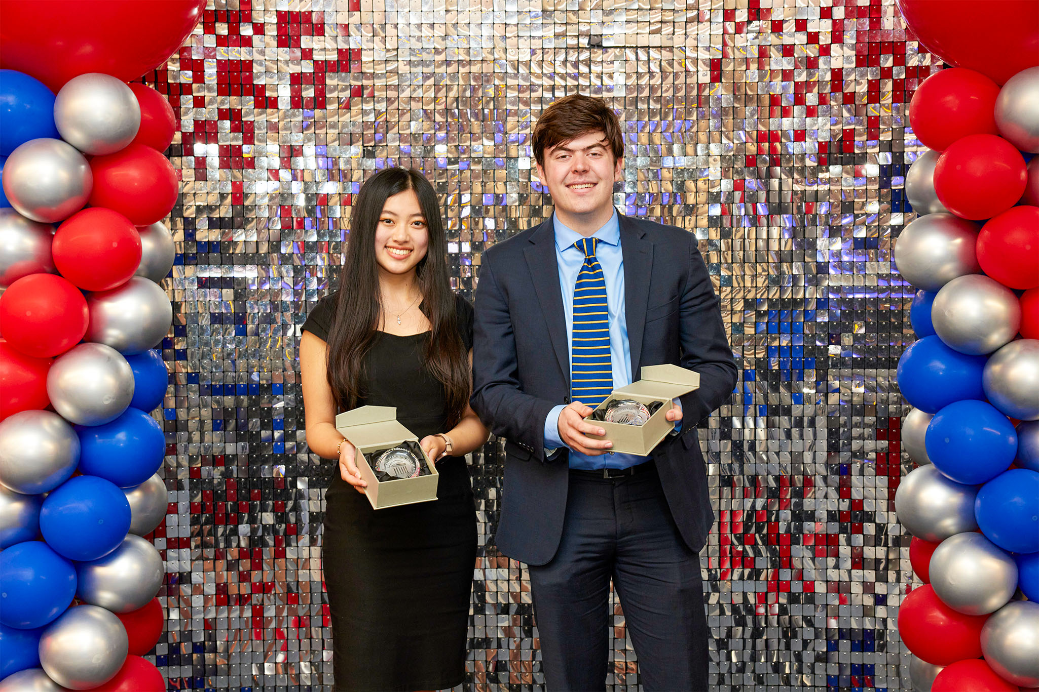 Outstanding Senior Awards Spring 2023, two students holding awards standing in front of silver backdrop with red, blue, and silver balloons