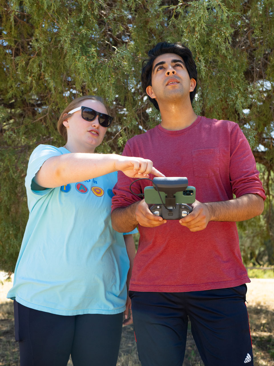 Two students standing looking up while holding a remote device for flying drones