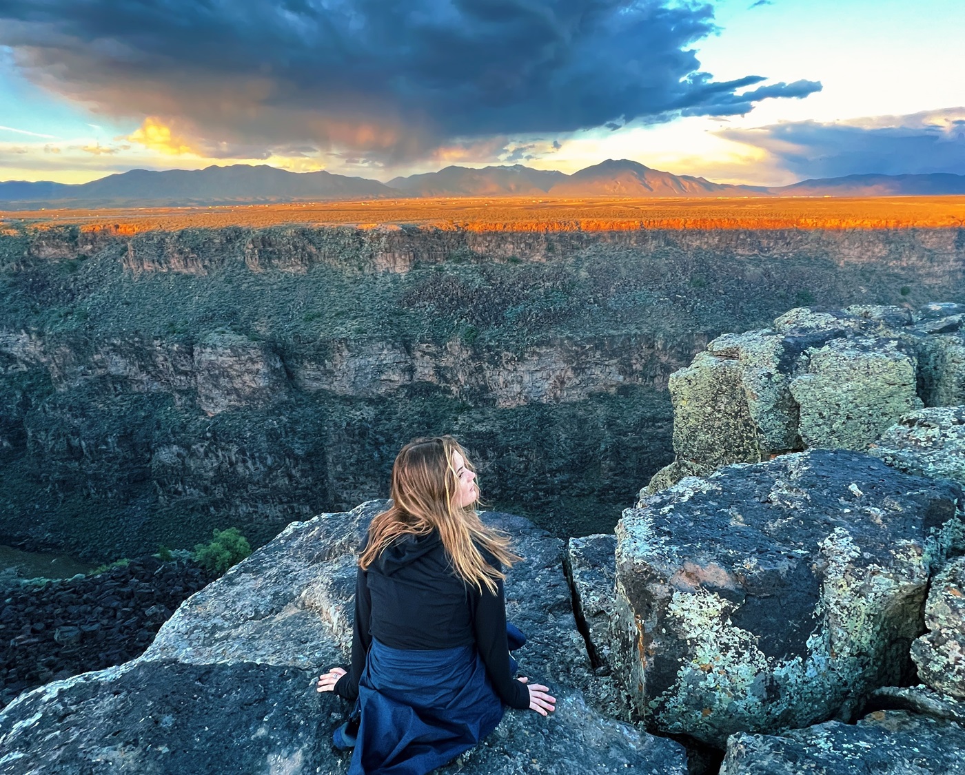 Student sitting over looking the Rio Grande Gorge with mountains and the sunset in the background