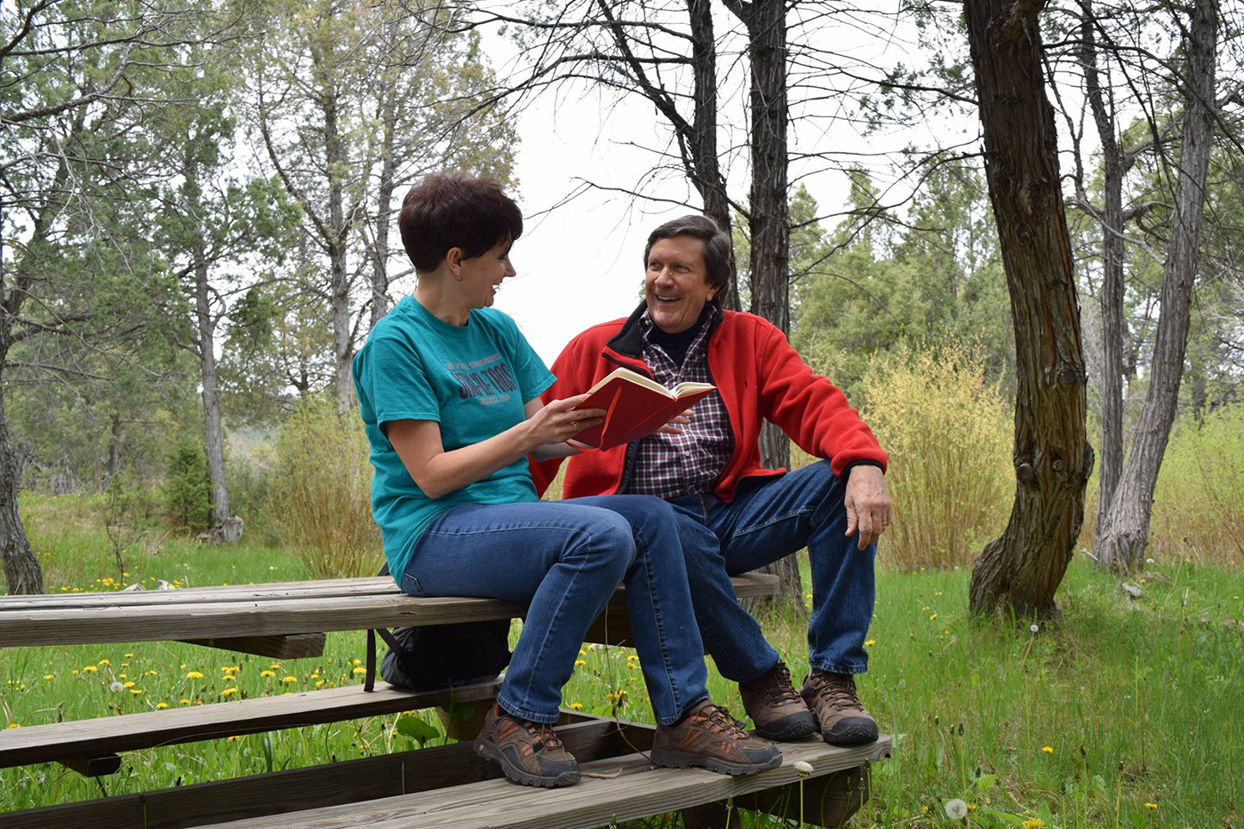 Two SMU-in-Taos faculty members sit on a picnic table discussing a book