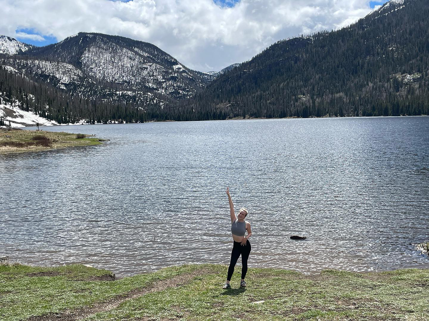 SMU-in-Taos student Ella Collard reaches overhead with one arm in front of a mountain lake in Taos, New Mexico. 