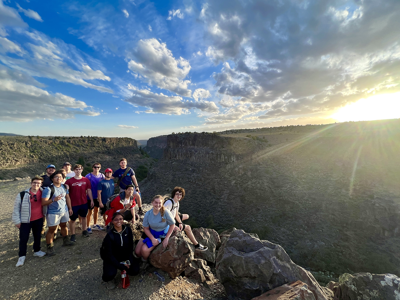 Group of Taos students gathered on a mountain as the sun sets in the distance.