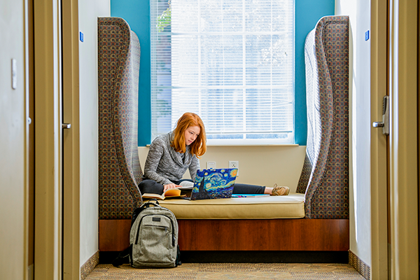 Student studying in a empty space inside the campus with books and a laptop, representing access to the SMU academic catalog.