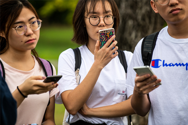 Three smu students standing holding there phone in their hand.