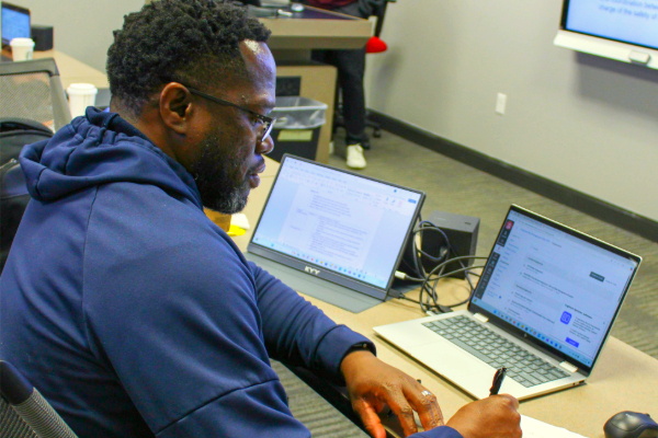 A student in the Weekend Format cohort at SMU Lyle School of Engineering takes notes during class while sitting in front of his open laptop.