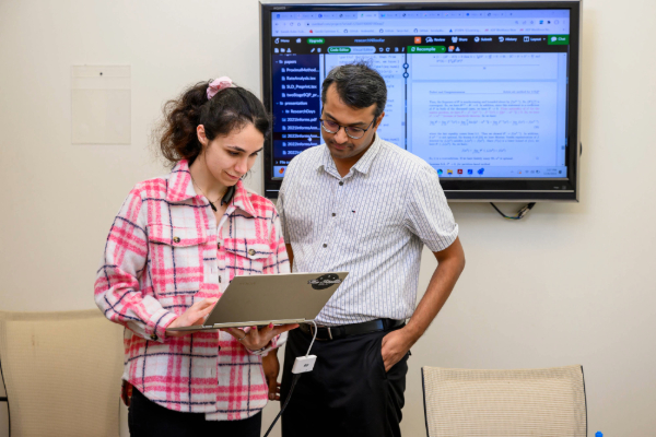 A student stands with her laptop beside SMU Lyle faculty member Harsha Gangammanavar, Ph.D.