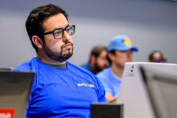 A student listens intently during a lecture at SMU Lyle School of Engineering and takes notes on his laptop.