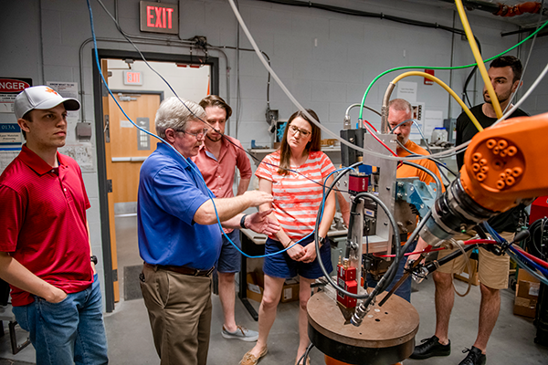 Students and faculty engaged in a hands-on engineering demonstration inside a laboratory, observing complex machinery.