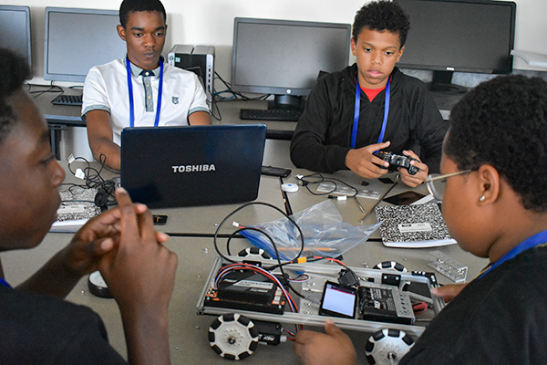 Group of boys working on robotics and electronics at a table with laptops and devices during an engineering camp