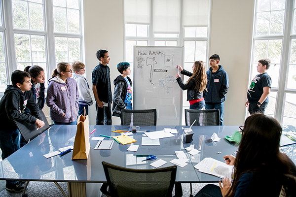 A student writes on a white board while others look on.