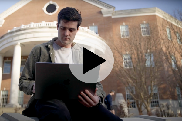 Founder Wilkie Stevens using a laptop in front of a university building for the Minerva project.