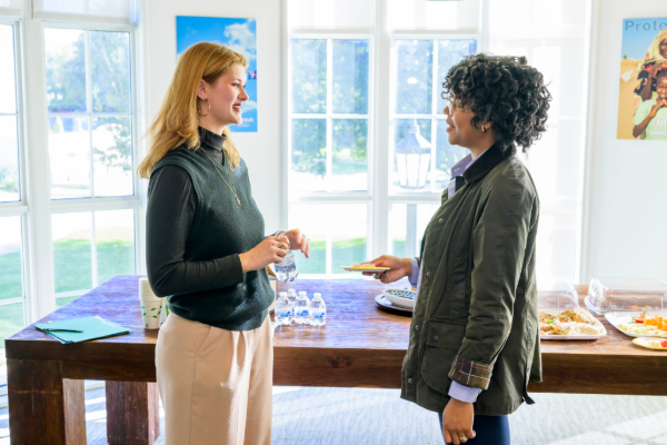A student and mentor are standing in a brightly lit room discussing something pleasantly