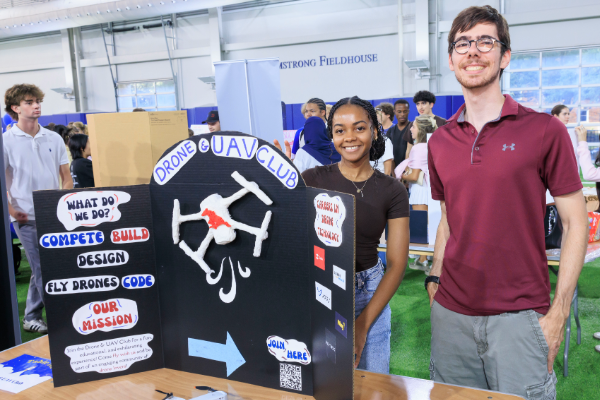 Two smiling students stand behind a drone poster at an exhibit at Armstrong Fieldhouse at SMU in Dallas