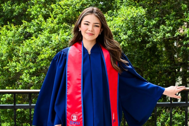 Brianna Navarro, mechanical engineering alum and Bell Flight defense engineer, stands outside in her SMU graduation robe after finishing her degree.