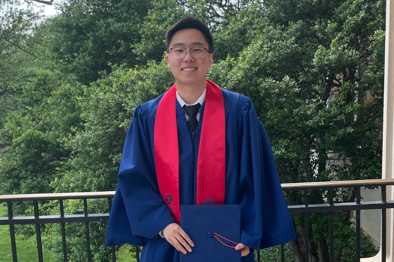Justin No, SMU Lyle Civil Engineering alumn, stands outside in his regalia on graduation day holding his cap