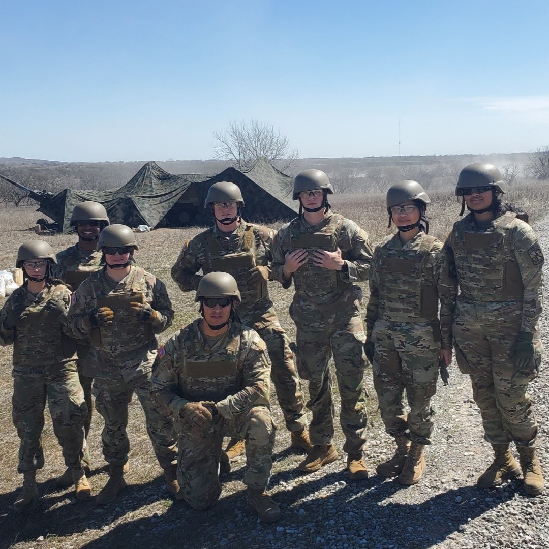A group of military people stand outside under the sun
