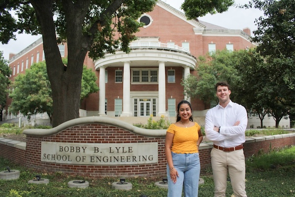 A female and male student stand smiling beside the Bobby B. Lyle School of Engineering at SMU on a nice day.