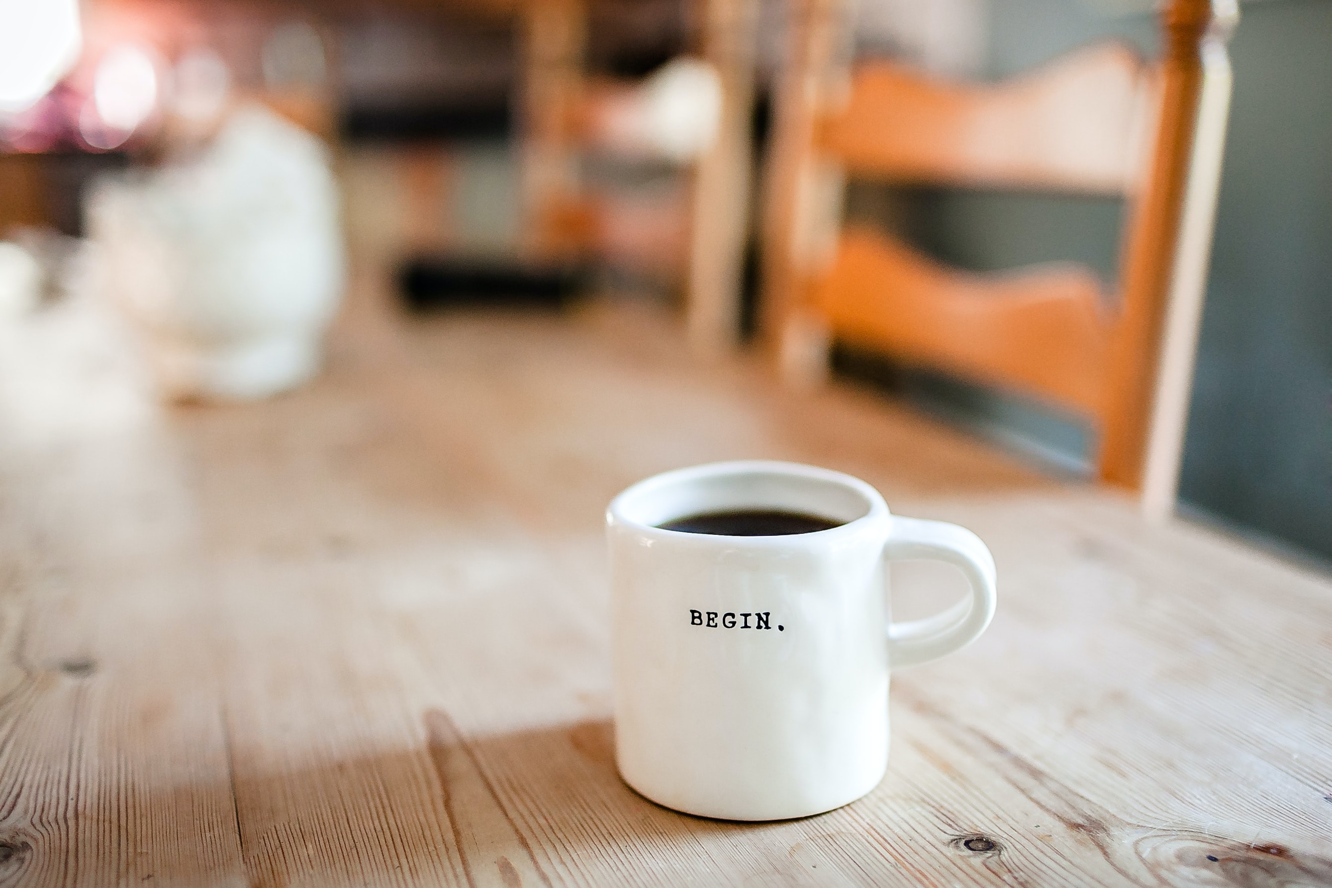 Coffee cup with the word "BEGIN." on it sits atop a wooden table.