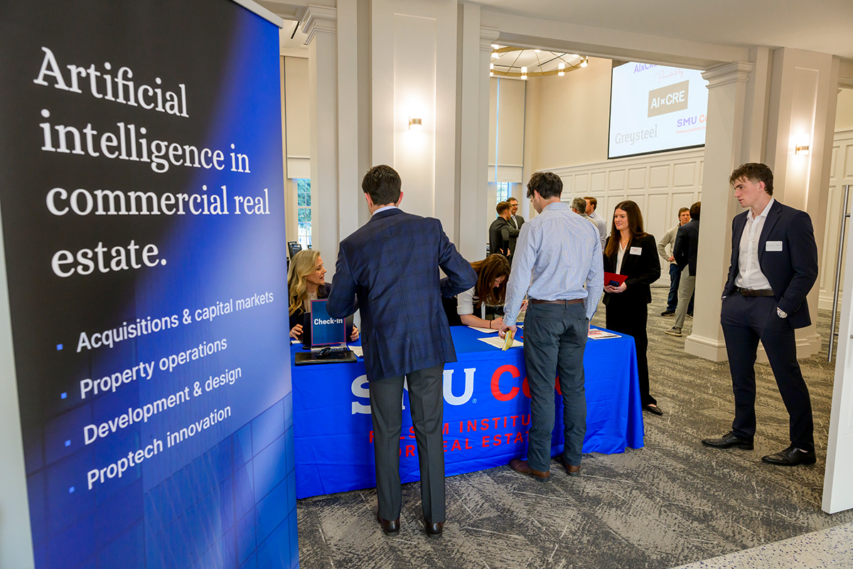 Attendees of an AI real estate conference gather around a registration table next to a sign that reads "Artificial intelligence is commercial real estate."