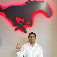 Zidan Thomas flashes the pony ears hand sign in front of a red neon SMU logo 