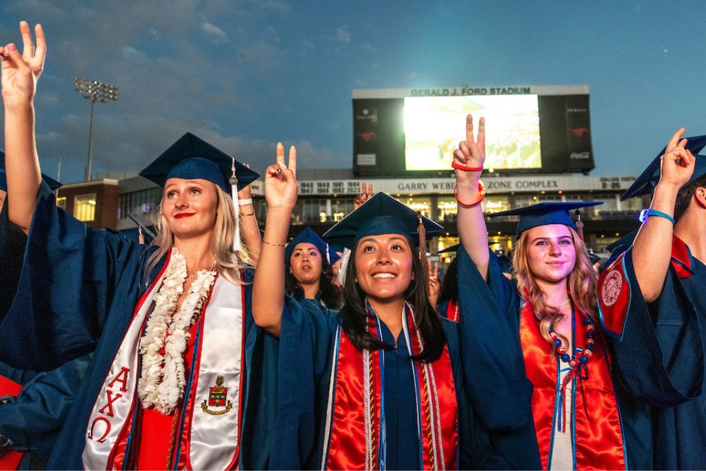Students standing at graduation with pony up raised in the air