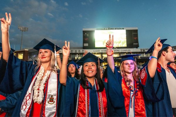 Crowd of students dressed in graduation attire standing outdoors in the evening
