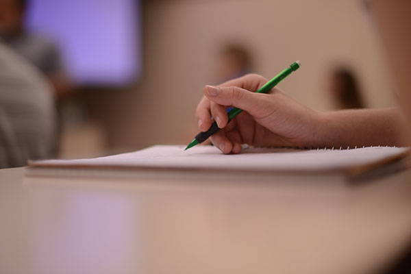 Photo of hand writing with pencil on paper.