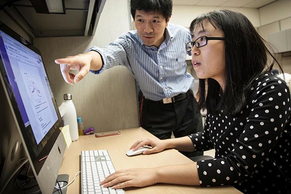 Two people looking at a computer, one is seated one is standing