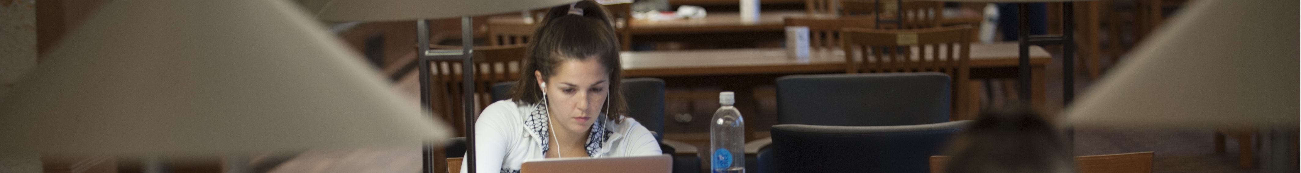 Student seated at table with laptop and headphones.