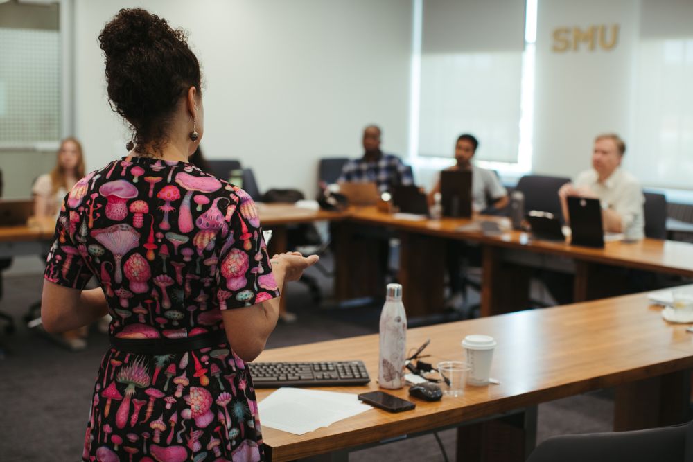 A woman presents in an SMU classroom with her back to the camera.