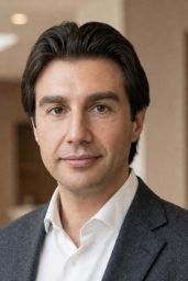 Dark haired man in a white collared shirt with blue suit jacket