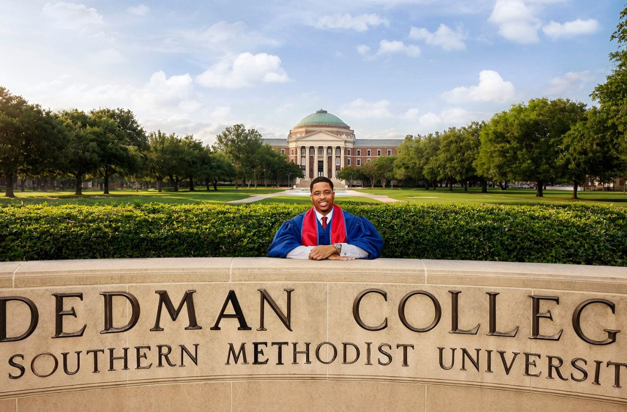 Chris Young dressed in cap and gown leaning on Dedman College outdoor sign