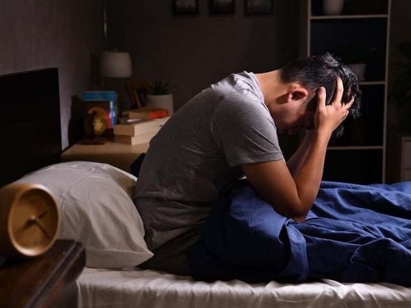 Young man sitting on bed with his head in his hands