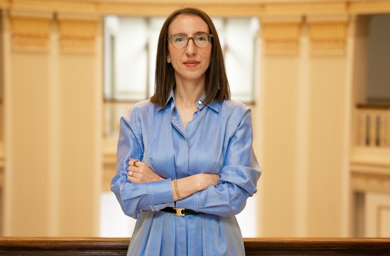 Olga Troitskaya with folded arms in Dallas Hall wearing a long sleeve blue dress