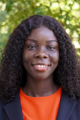 Sarah Bainm in an outside setting with orange shirt and navy blazer.