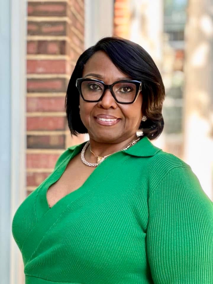 Headshot of Remonda Hammock wearing a green sweater shirt with dark rimmed glasses.