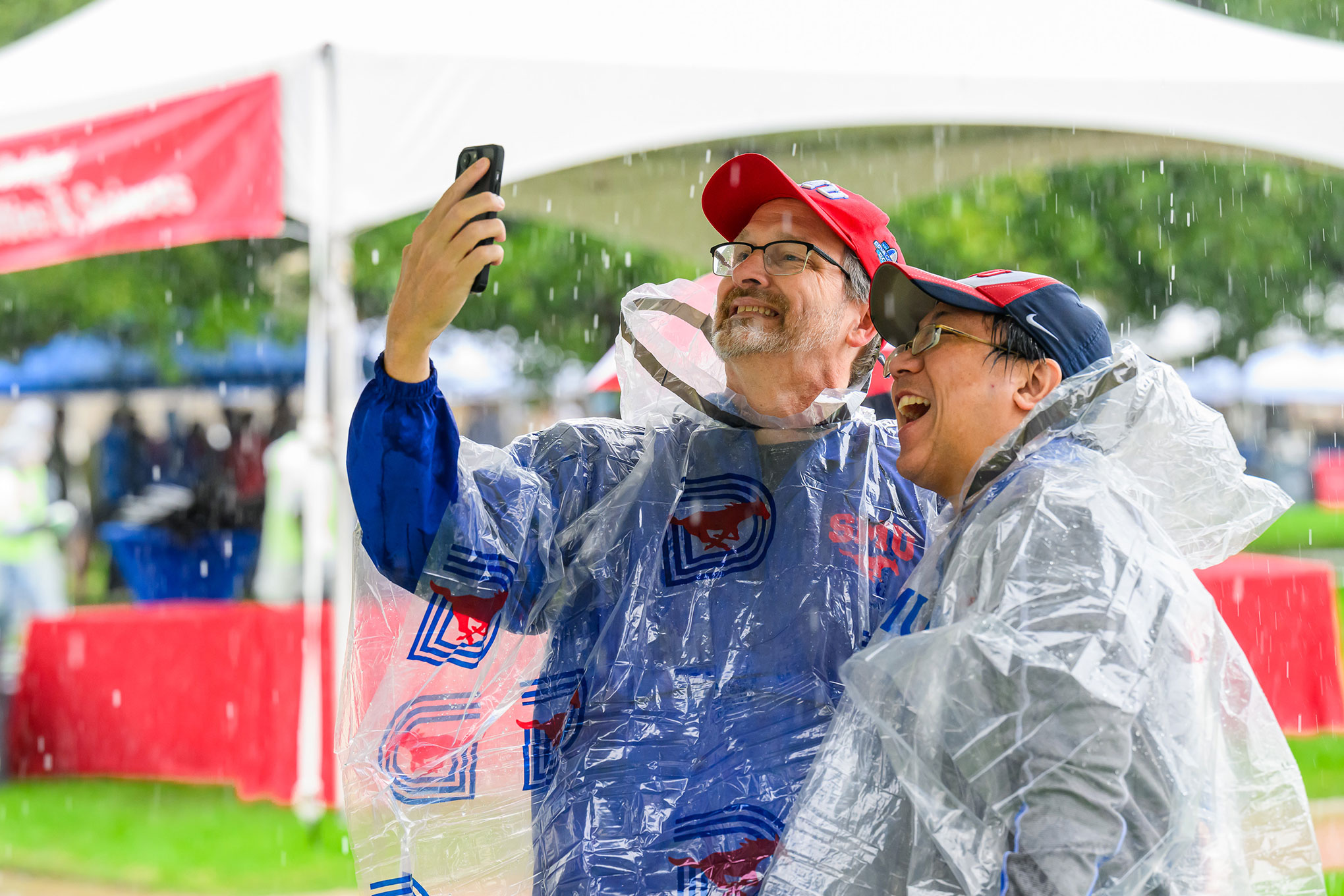 SMU alumni wearing ponchos take a selfie during a rain shower