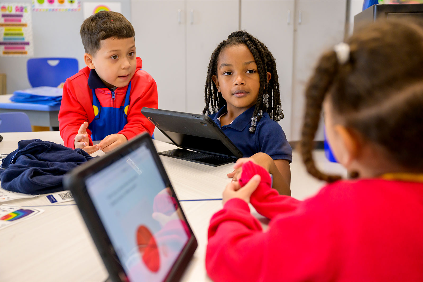 Three children interact with each other while viewing images on an electronic tablet.