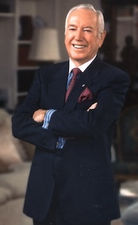 Robert Dedman Sr, an older white man wearing a dark suit, smiling while standing in a warmly lit room