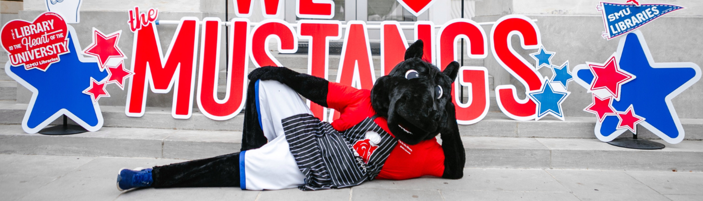 Peruna mascot lays across the Fondren Library steps in front of colorful signs