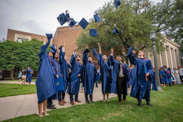 Cox students in SMU graduation regalia throwing their caps in the air 