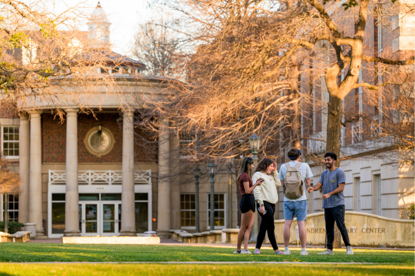 Four students talk in front of Fondren Library