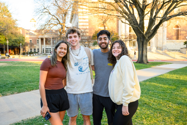Four students stand with arms around each other in front of Fondren Library