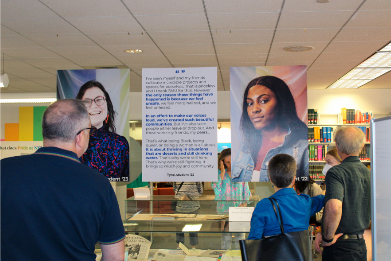 Several people reading a poster from the In Search of Belonging exhibit