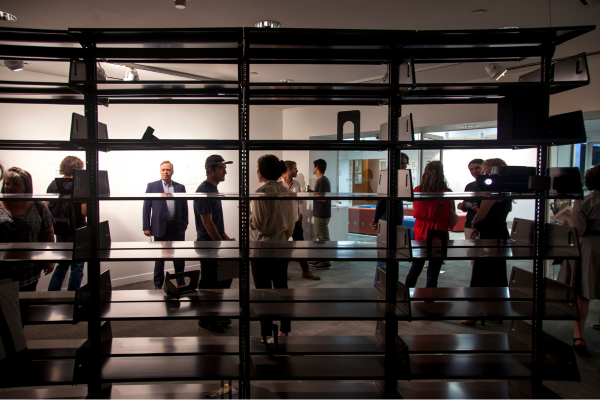 Many people in a darkened room, seen from behind a shelf