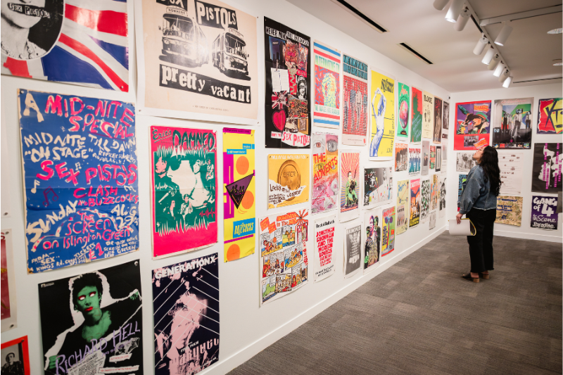 A woman looks at art in a room covered in colorful band posters