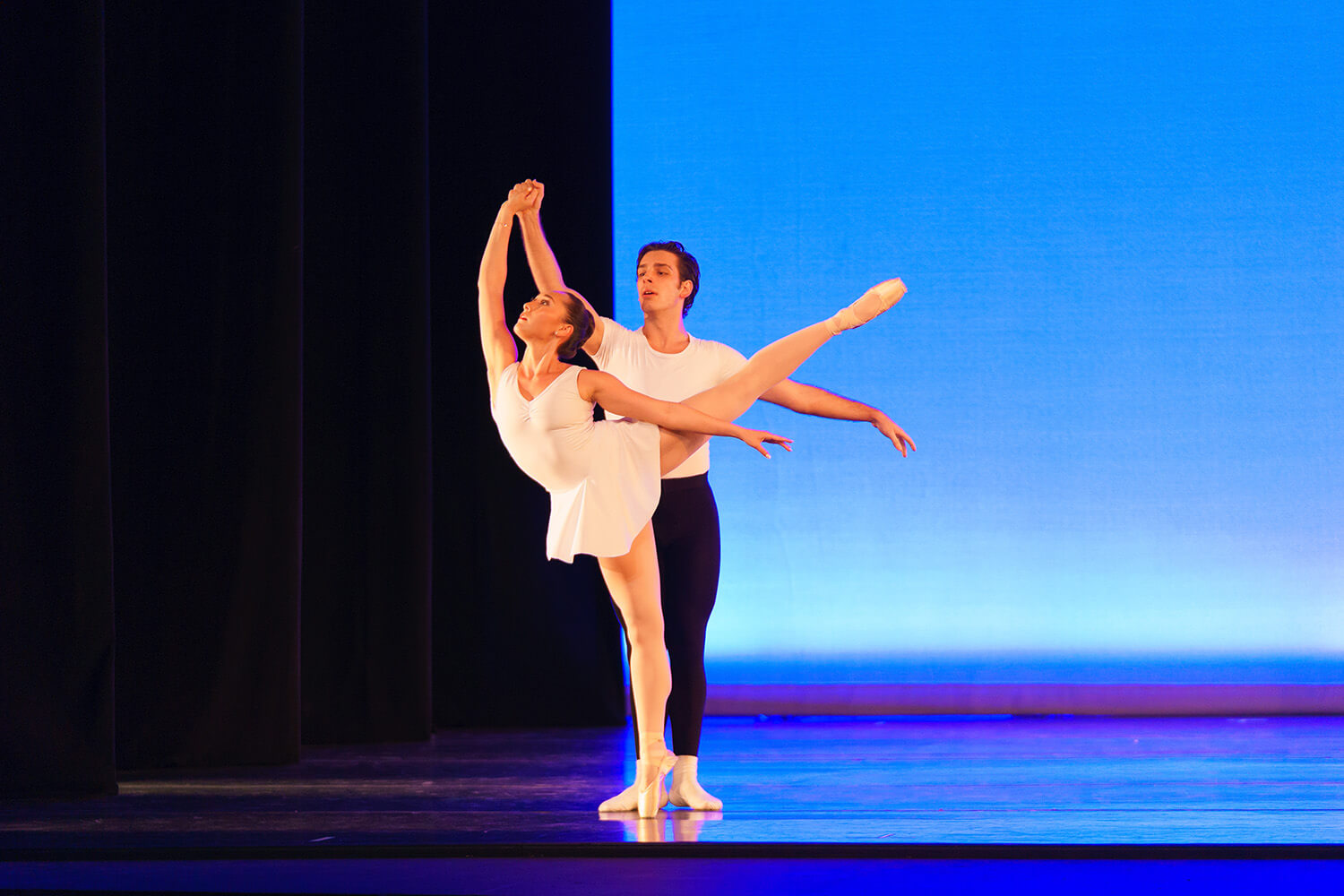 male and female dancers on stage dressed in white with blue back ground