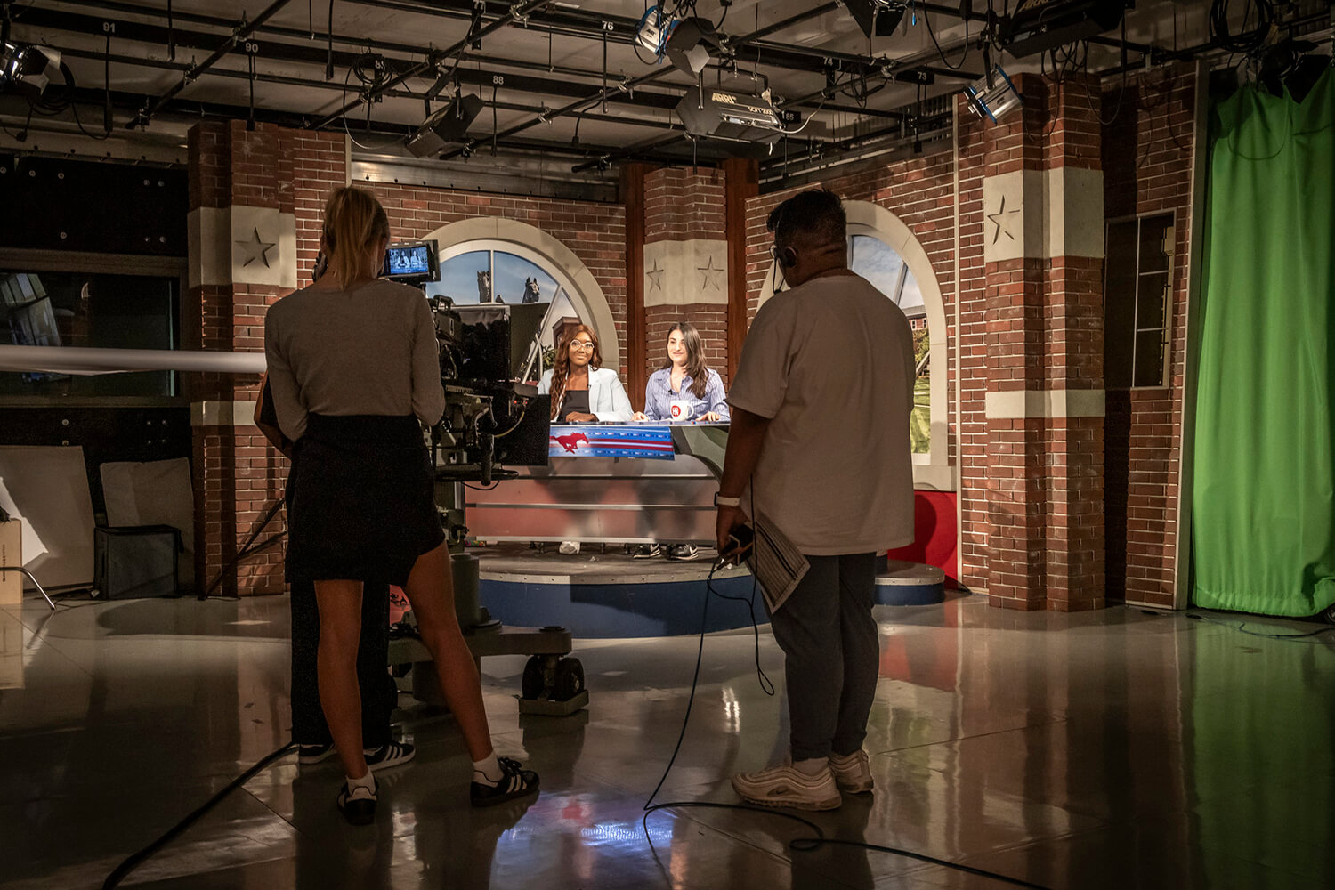 two students behind the scenes of a news desk studio