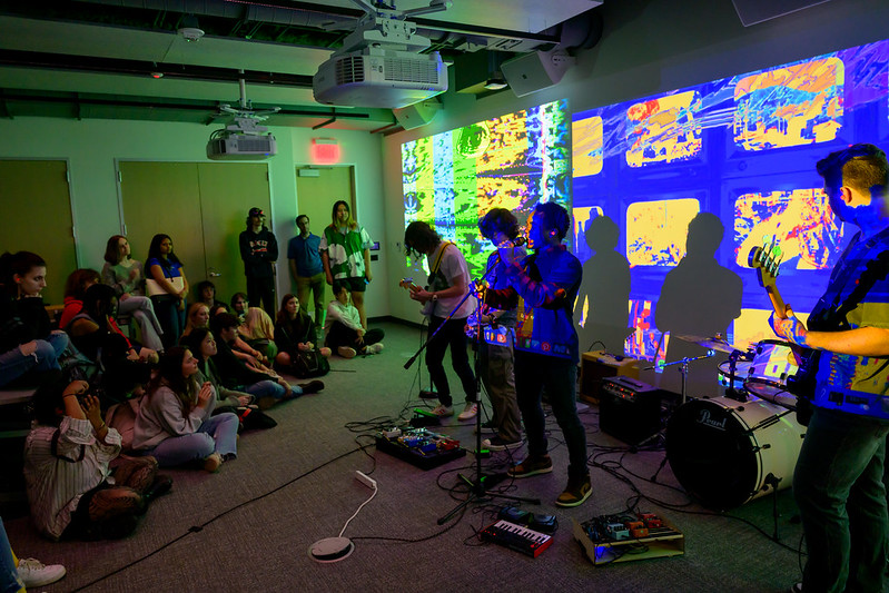 Creative computation students play instruments in front of the digital backdrop